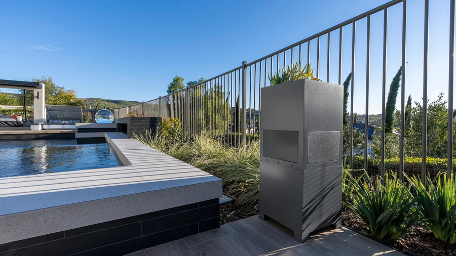 Outdoor landscape speaker installed beside a modern pool and patio, blending into the landscape.
